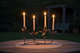 Brass 4 Candle holder with four lit candles on a wooden surface at night.